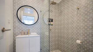 Ein Badezimmer mit Dusche, Waschbecken und Spiegel, sowie einem gemusterten Boden.