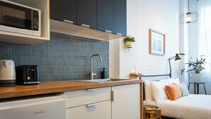 Eine kompakte Küche mit Mikrowelle, Toaster und Spüle. Ein Bett mit Kissen und ein Nachttisch mit Lampe.
