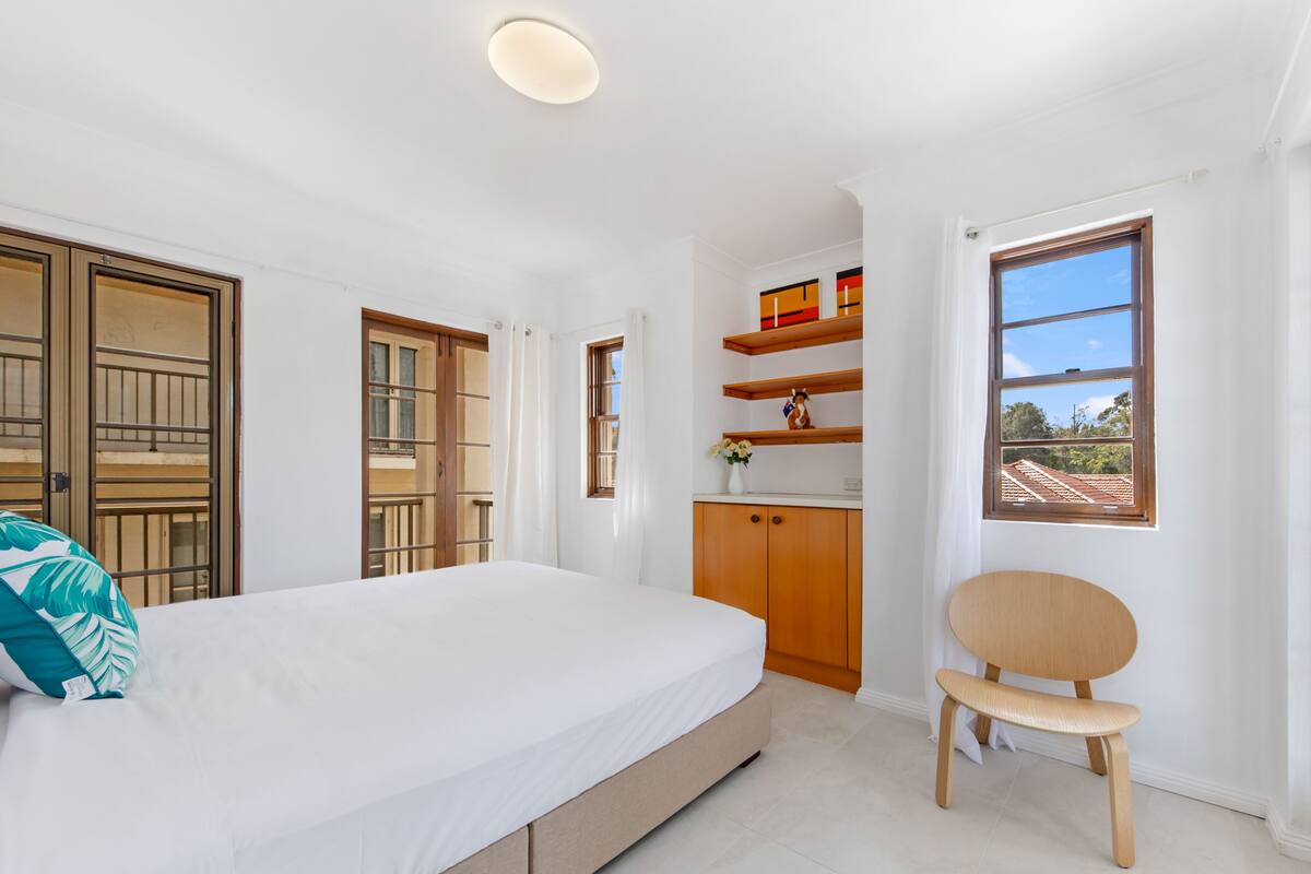 A bedroom with a bed, wooden wardrobe, shelves, and a window with a view.