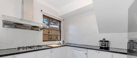 A modern kitchen with white cabinets, a black countertop, a built-in stove, a window with a view, and a rice cooker.