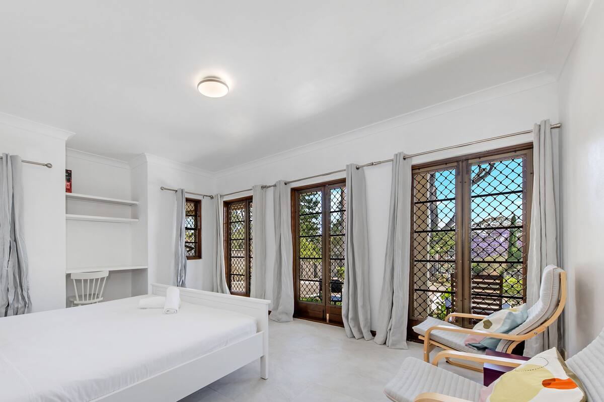A bedroom with a bed, a chair, a shelf, and a window with curtains.