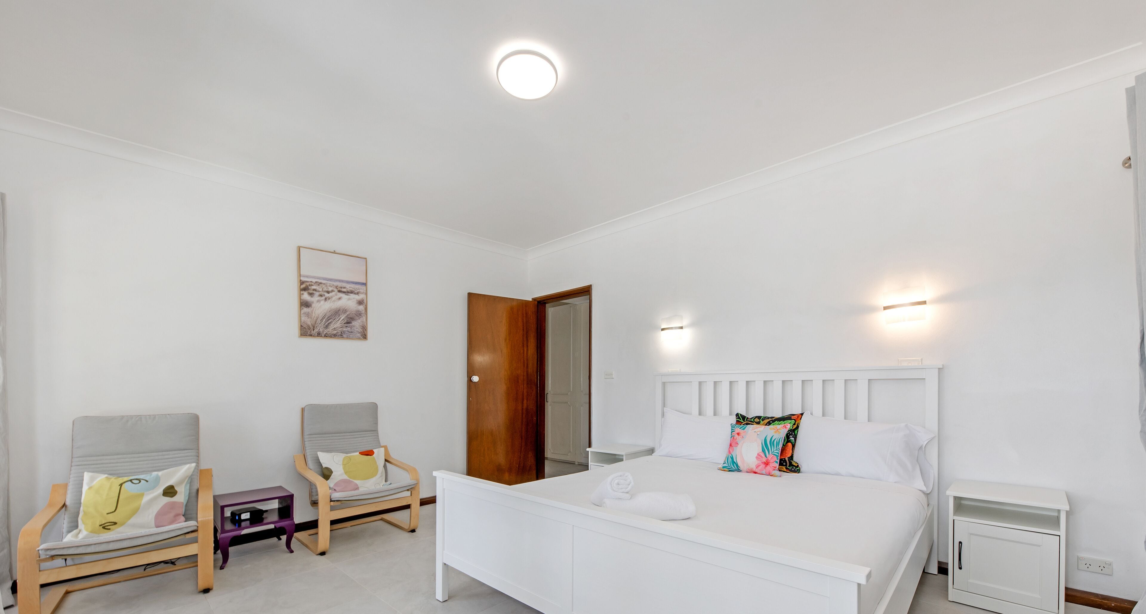 Une chambre à coucher avec un lit, deux chaises, une table de chevet et une porte.