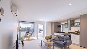 Un apartamento moderno con sala de estar, comedor y cocina. Cuenta con ventanas grandes, un balcón y vistas a la ciudad.