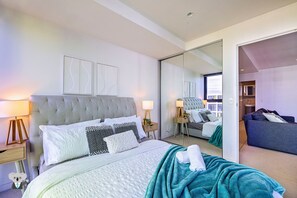 Una habitación de hotel moderna con una cama grande, un espejo, una zona de estar y un armario.