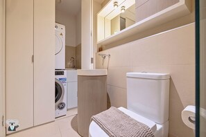 Un baño pequeño con lavadora, inodoro, lavamanos y un espejo sobre el lavamanos.