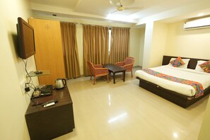 A hotel room with a bed, a desk with a chair, a television, and an air conditioning unit.