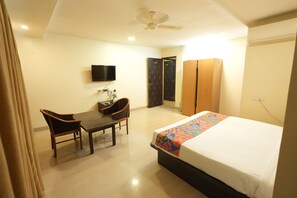 A hotel room with a bed, a desk, two chairs, a television, and a wardrobe.