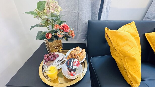 Aamiaistarjotin, jossa on croissantteja, viinirypäleitä, appelsiinimehua ja proteiinipitoinen juoma, ja kaikki on aseteltu kultaiseen tarjottimeen.