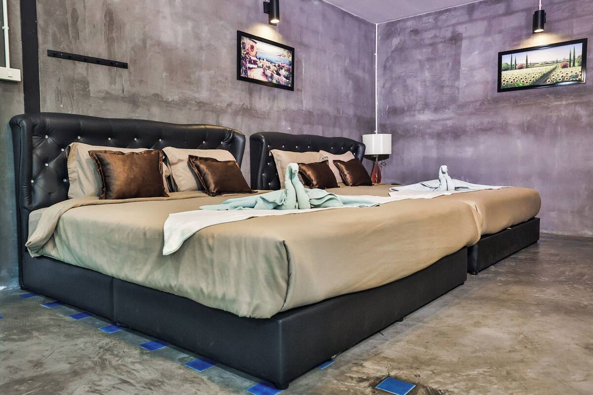 Una cama doble con colcha color beige y marrón, dos cabeceros negros y una pequeña estatua sobre la mesita de noche.