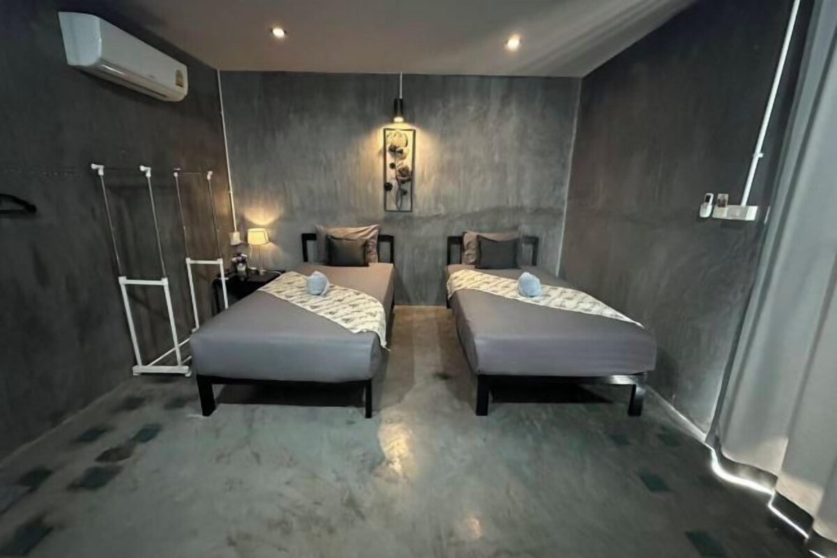 Een kamer met twee bedden, een staande lamp, een luchtverkoeler aan de muur en een ingelijst schilderij.