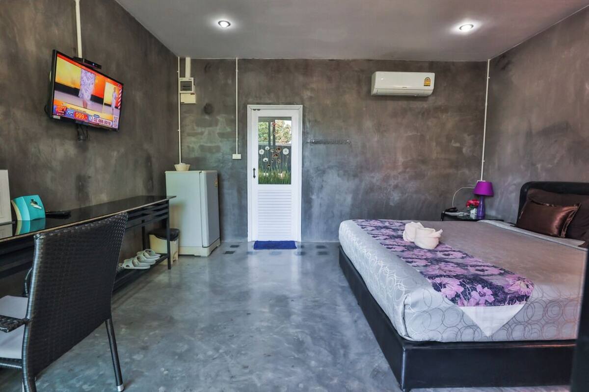 Una habitación de hotel moderna con cama, escritorio, silla, televisor y unidad de aire acondicionado.
