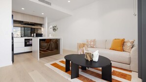 A modern living room with a sofa, a coffee table, and a kitchen area visible through an open door. - Queens Wharf Gem Stylish 1BR in BNEsNew Landmark (Brisbane City)