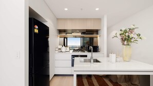 A modern kitchen with a black refrigerator, white cabinets, and a central island with a sink. - Queens Wharf Gem Stylish 1BR in BNEsNew Landmark (Brisbane City)
