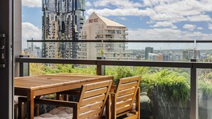 A balcony with a wooden table and chairs, overlooking a cityscape with modern buildings and a clear sky. - Queens Wharf Gem Stylish 1BR in BNEsNew Landmark (Brisbane City)