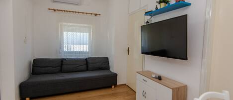 A modern living room with a grey sofa, wooden flooring, a mounted TV, and a white cabinet.