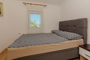Un dormitorio con una cama, una ventana con cortina, una mesita de noche y un velador.