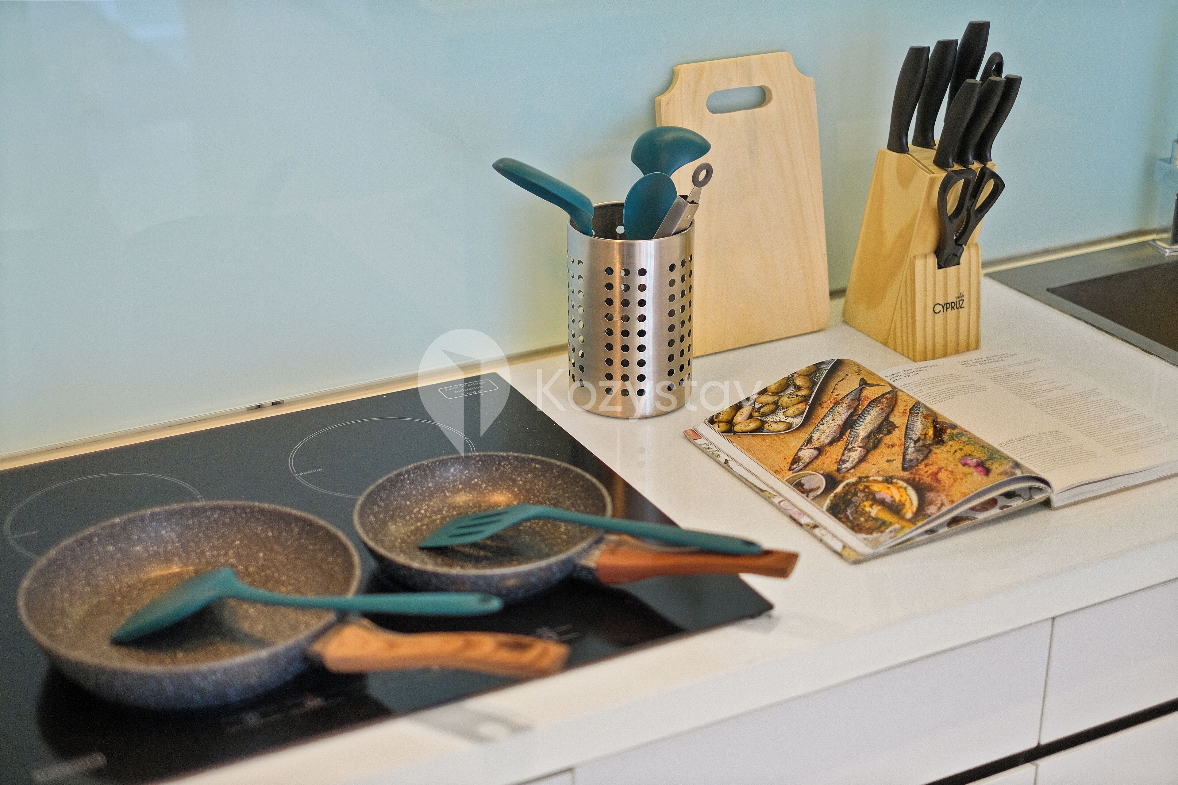 A kitchen counter with two frying pans, a grater, a wooden cutting board, and a knife block.