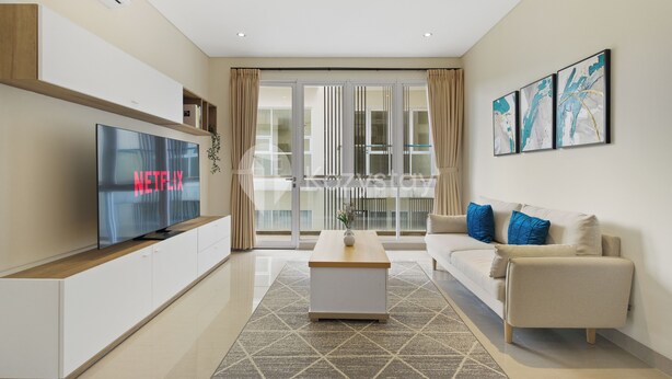 Een moderne woonkamer met een flatscreen televisie, een houten salontafel, een beige bank met blauwe kussens en een groot raam met gordijnen.