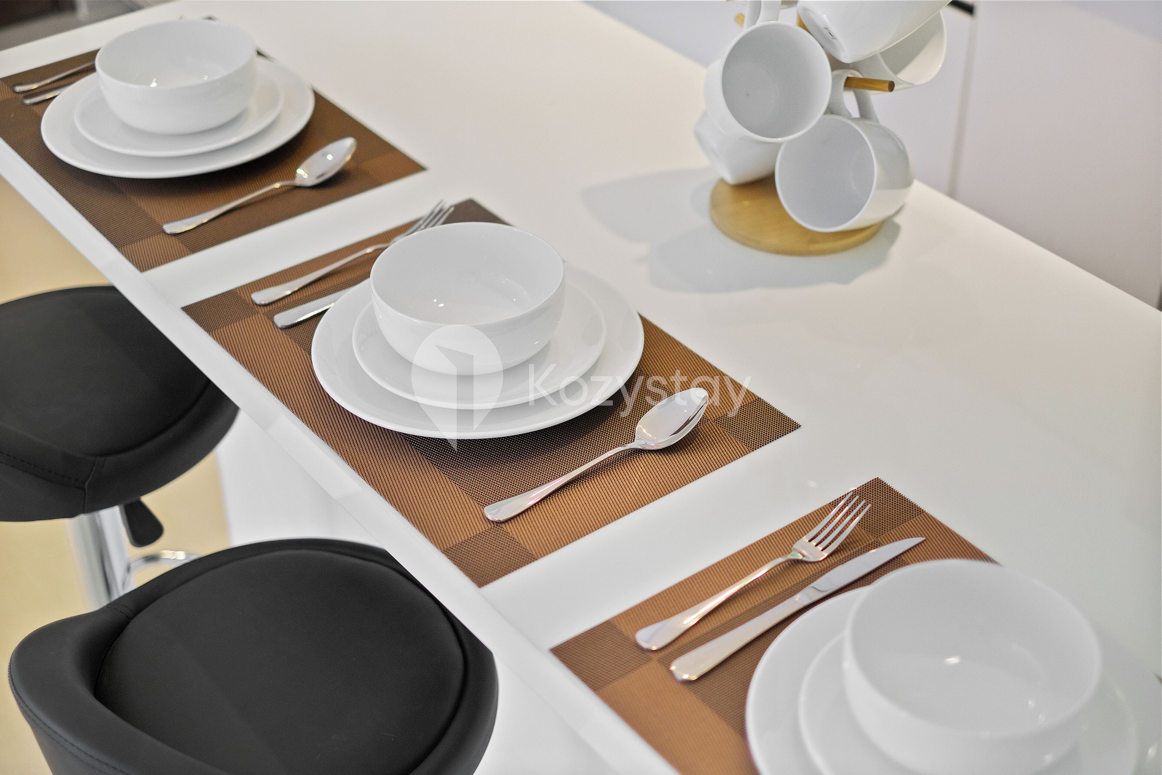 A dining table set with white plates, bowls, cutlery, and a stack of white cups.