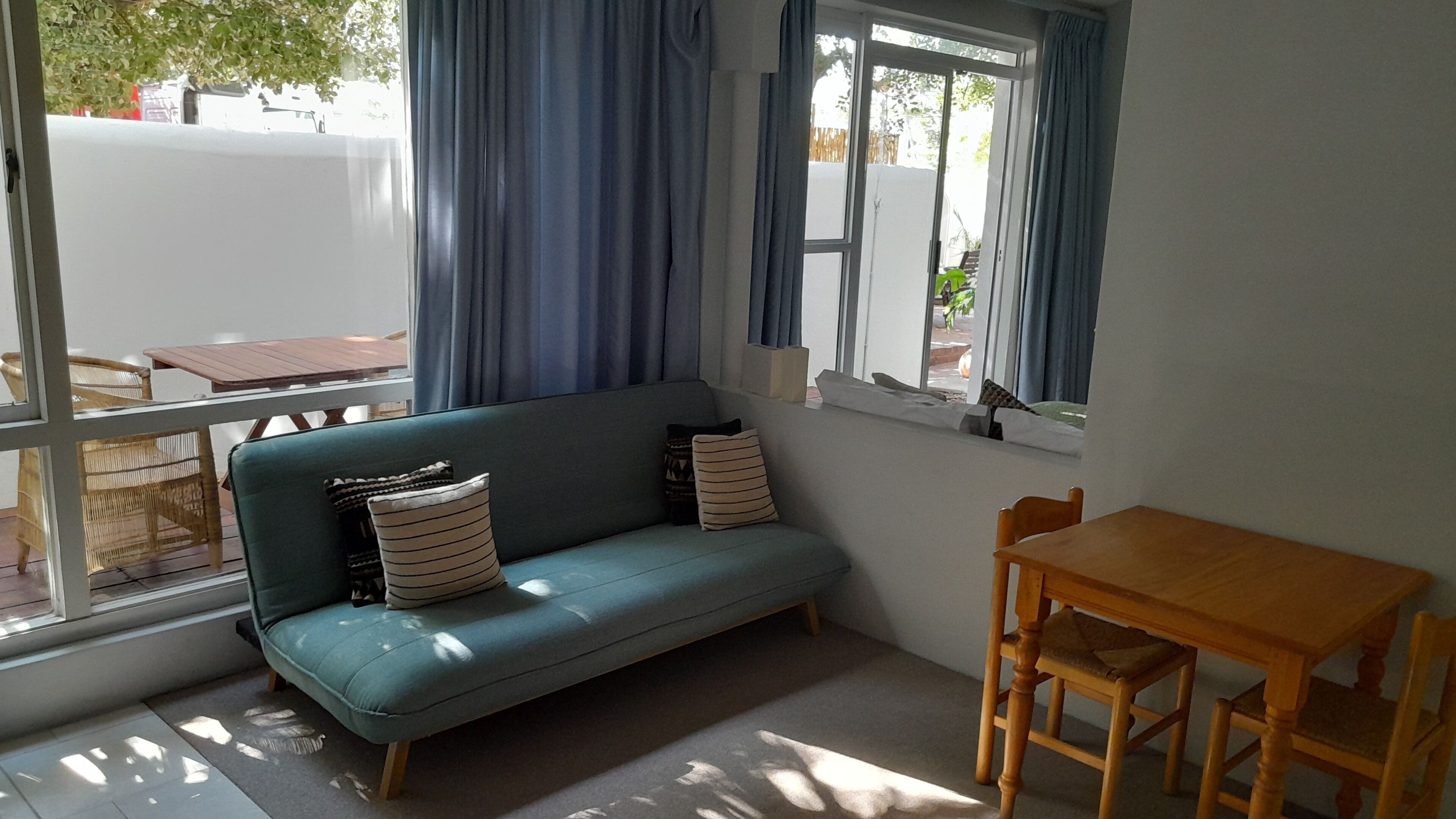 A room with a teal sofa, two pillows, a wooden table, and a chair.
