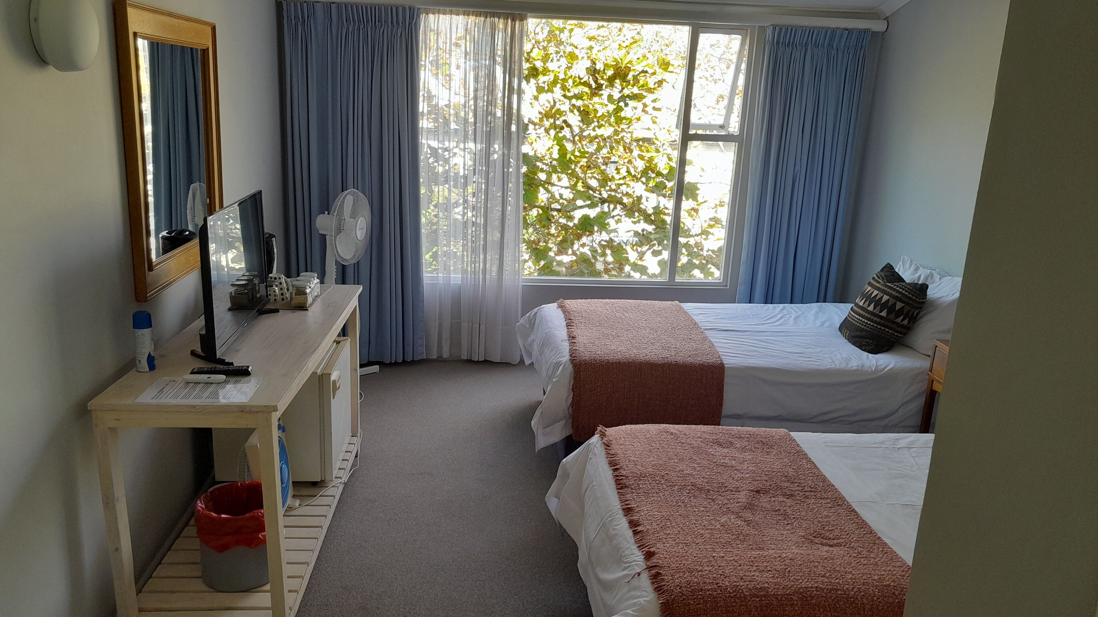 A hotel room with two beds, a desk with a computer, a mirror, and a window with curtains.