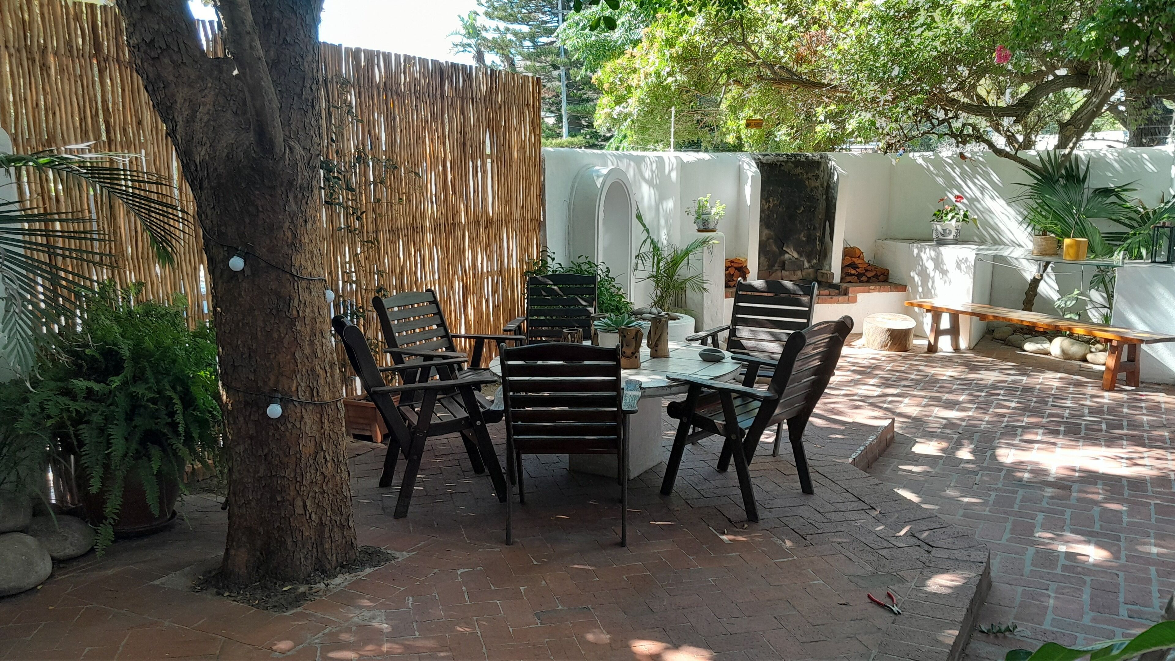 An outdoor patio with a brick floor, wooden chairs, a table, and potted plants.