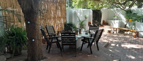 An outdoor patio with a brick floor, wooden chairs, a table, and potted plants.