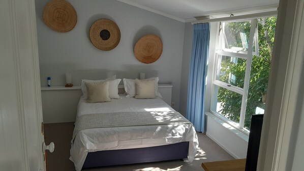 Ein Schlafzimmer mit Bett, Kissen, Nachttisch, einem Fenster mit Vorhängen und Wanddekoration.