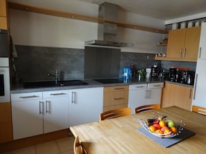 A modern kitchen with white cabinets, a black countertop, and a stainless steel range hood. There is a fruit bowl on the table and a coffee maker on the counter. - Warm, child-friendly home with swimming pool and vegetable garden (La Garde)
