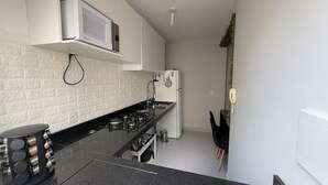 Una cocina moderna con armarios blancos, encimera negra, microondas, estufa y refrigerador.