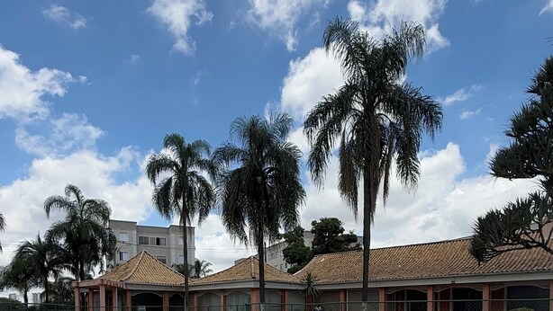Una piscina con sillas de descanso, palmeras y un edificio con techo de tejas.
