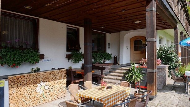 An outdoor patio with a checkered table, wicker chairs, and a wooden log wall. - Alpenhotel Waidmannsheil (Bad Hindelang)