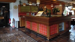 Een receptie met een houten balie, betegelde vloer, hangende lampen en plantenpotten.