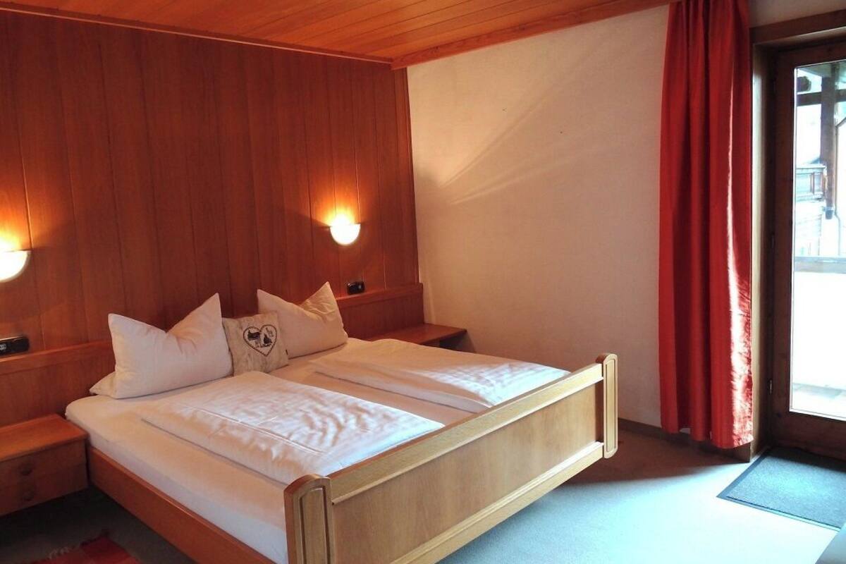 Cama de madeira com roupa de cama branca, duas mesas de cabeceira e luminárias fixadas na parede.