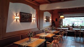 A restaurant interior with wooden tables, cushioned benches, and wall-mounted lamps. - Alpenhotel Waidmannsheil (Bad Hindelang)