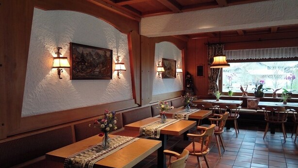 Een restaurant interieur met houten tafels, beklede banken en wandlampen.