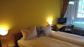 Een hotelkamer met een tweepersoonsbed, twee bedlampen, een bureau met een computer en een stoel.