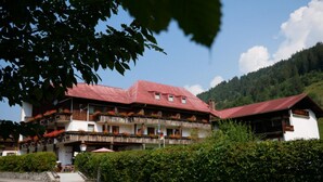 Een hotel met meerdere verdiepingen, balkons, een rood dak en een bergachtige achtergrond.