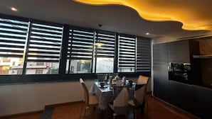 Un'area pranzo con tavolo apparecchiato per quattro, ampie finestre con tende e una zona cucina sul lato destro, con un design di soffitto curvo.