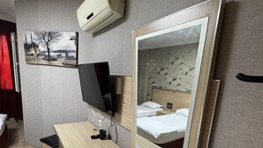 A hotel room with a wooden desk, a television, a bed with a headboard mirror, and a wall-mounted air conditioner. - Adana Madi Hotel (Adana)
