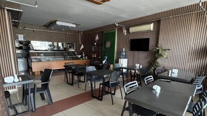 A restaurant with a counter, multiple tables, and chairs. There is a green door and a wall-mounted TV. - Adana Madi Hotel (Adana)