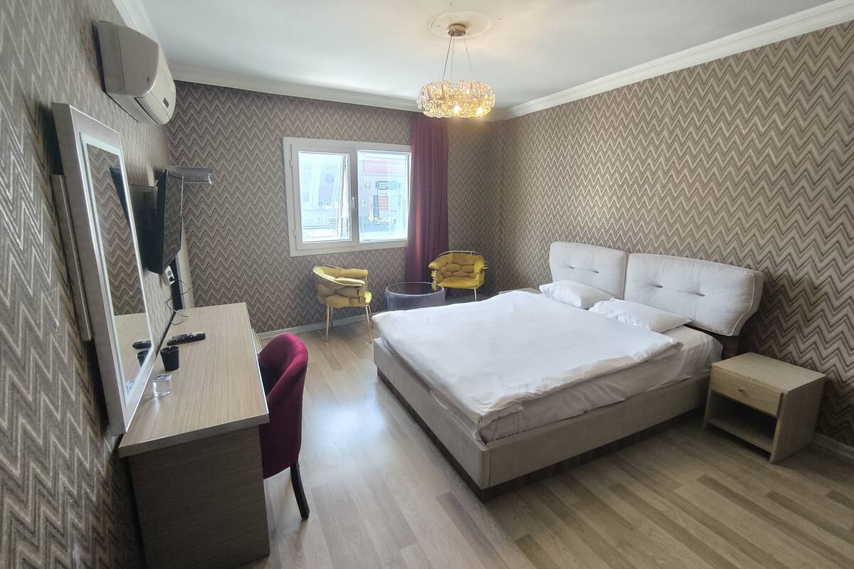 Una habitación de hotel con una cama grande, un escritorio con silla, televisor y ventana con cortinas.