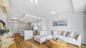 Una sala de estar moderna con un sofá seccional de color gris claro, una mesa de centro de madera y una cocina al fondo.