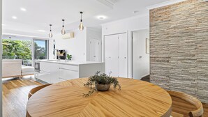 Una cocina moderna con armarios blancos, una mesa de comedor de madera e iluminación colgante.