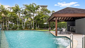 Una piscina con hidromasaje, rodeada de palmeras y un área de patio techada.