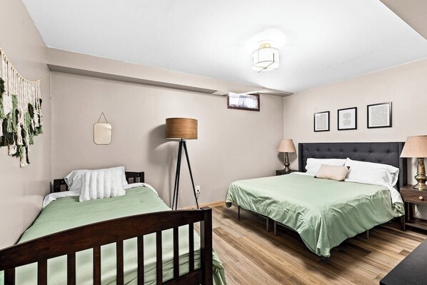 A bedroom with two beds, a hanging lamp, framed pictures on the wall, and a ceiling light. - The Gathering House (Superior)