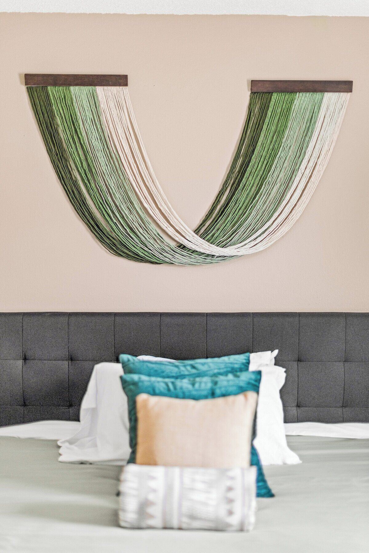 A bedroom with a grey upholstered headboard, a bed with white and teal bedding, and a hammock hanging from the ceiling.
