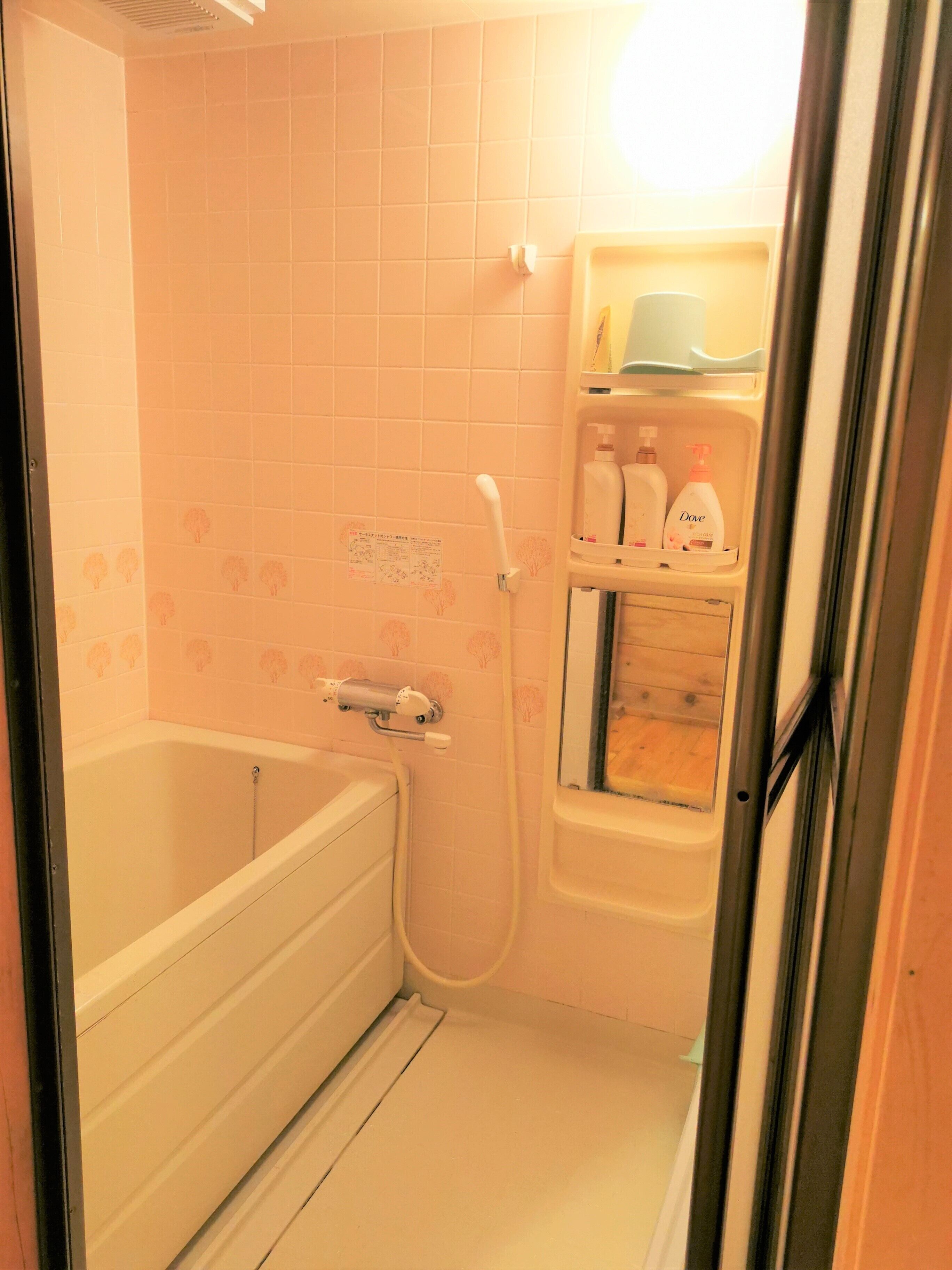 A bathroom with a bathtub, a shower, and a shelf with toiletries.