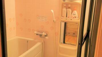 A bathroom with a bathtub, a shower, and a shelf with toiletries.