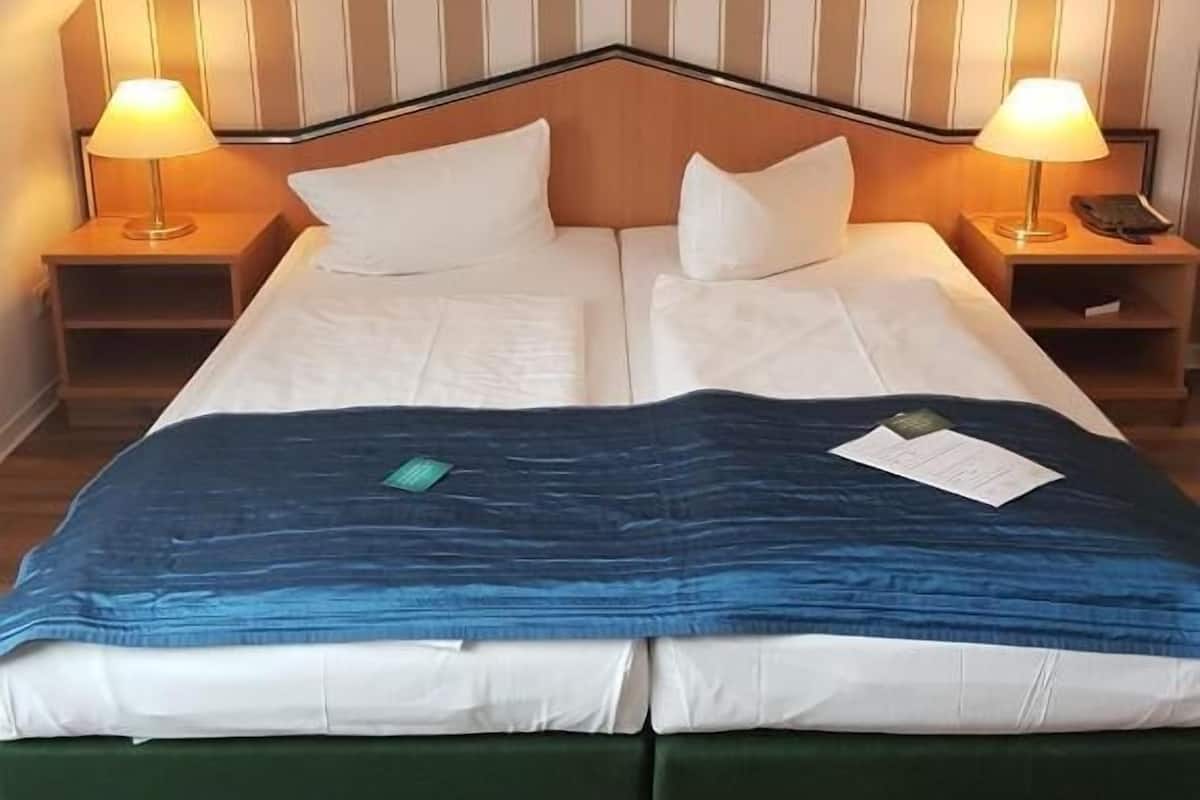 A double bed with a blue blanket, two pillows, and a wooden headboard. There are two bedside tables with lamps.